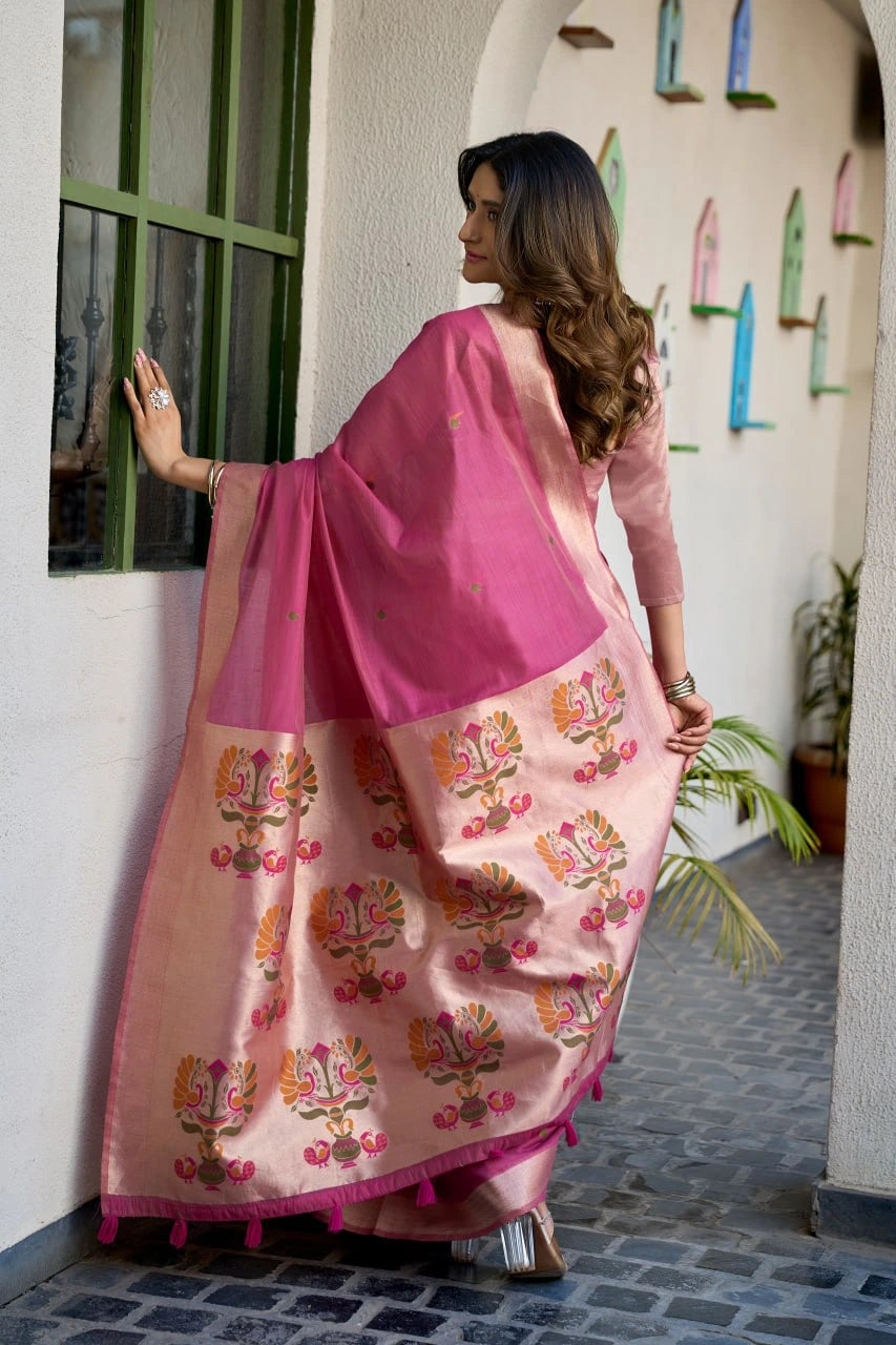 Woman in a pink saree with floral patterns standing against a wall.